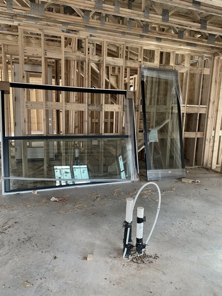 Interior framing with large glazing units leaning against it, and PVC stub-ups standing on the slab.