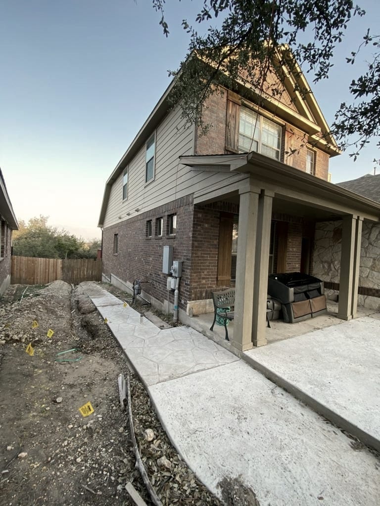A two-story brick and siding house at dusk, with a trench and yellow utility marker flags along the side.