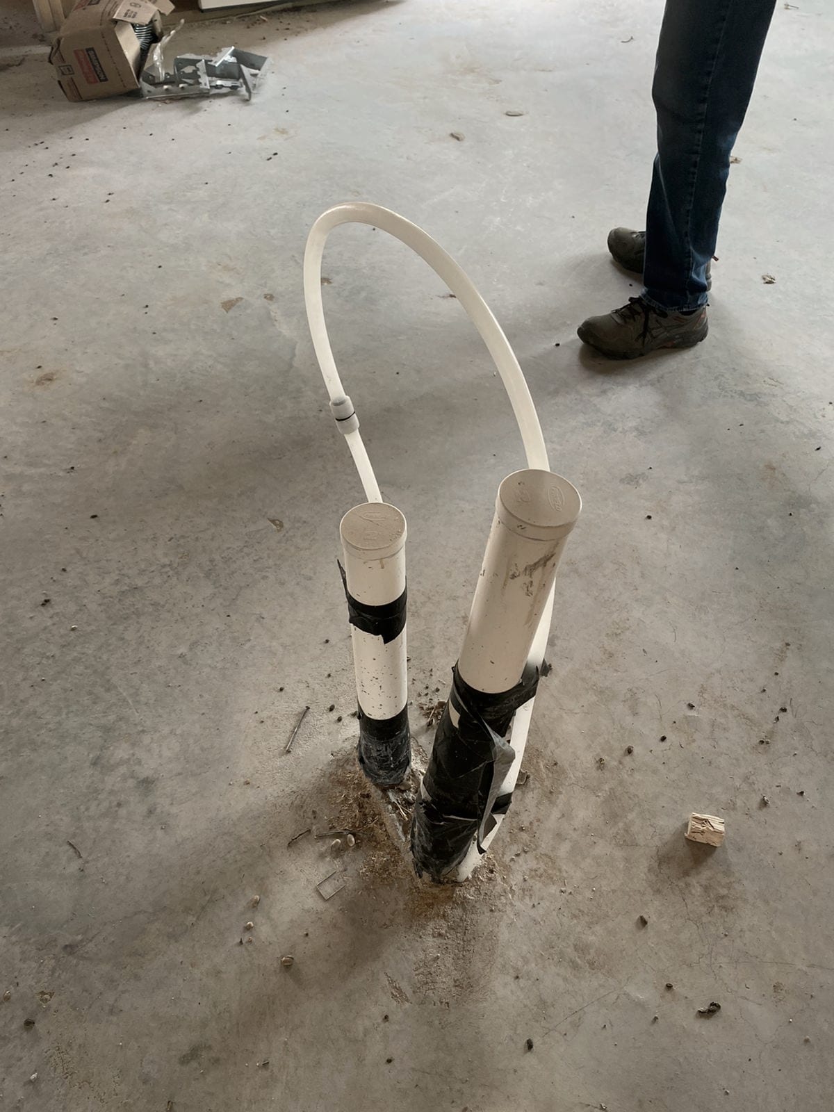 Two capped PVC stub-ups and a looped line rising through a bare concrete slab.
