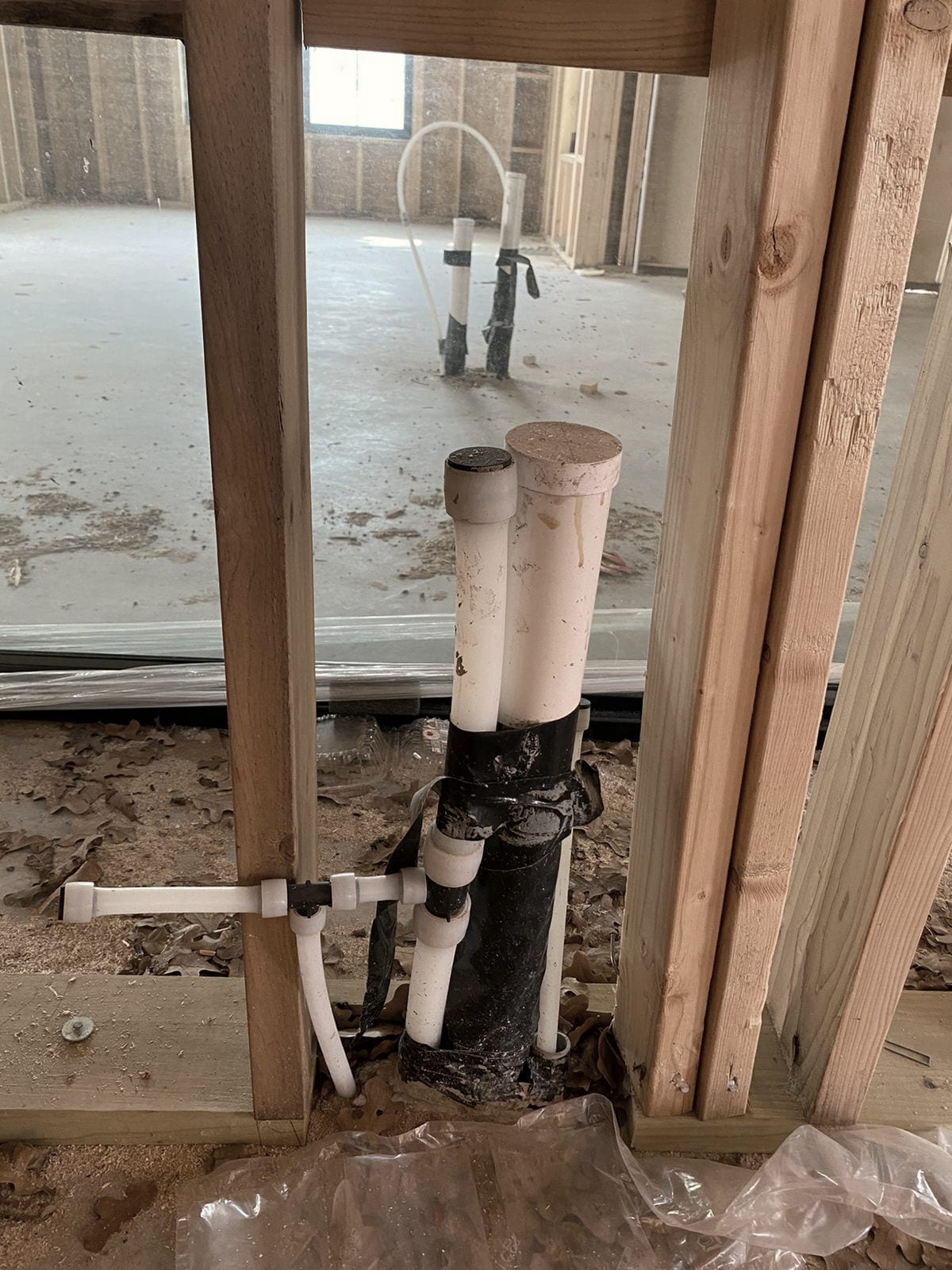A stack rising through the slab between wall studs, damp sawdust and sheeting around its base.