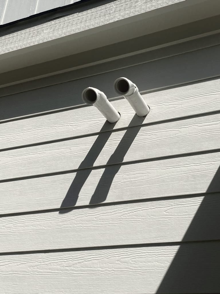 Two white pipe stubs standing out through pale siding, casting hard shadows.